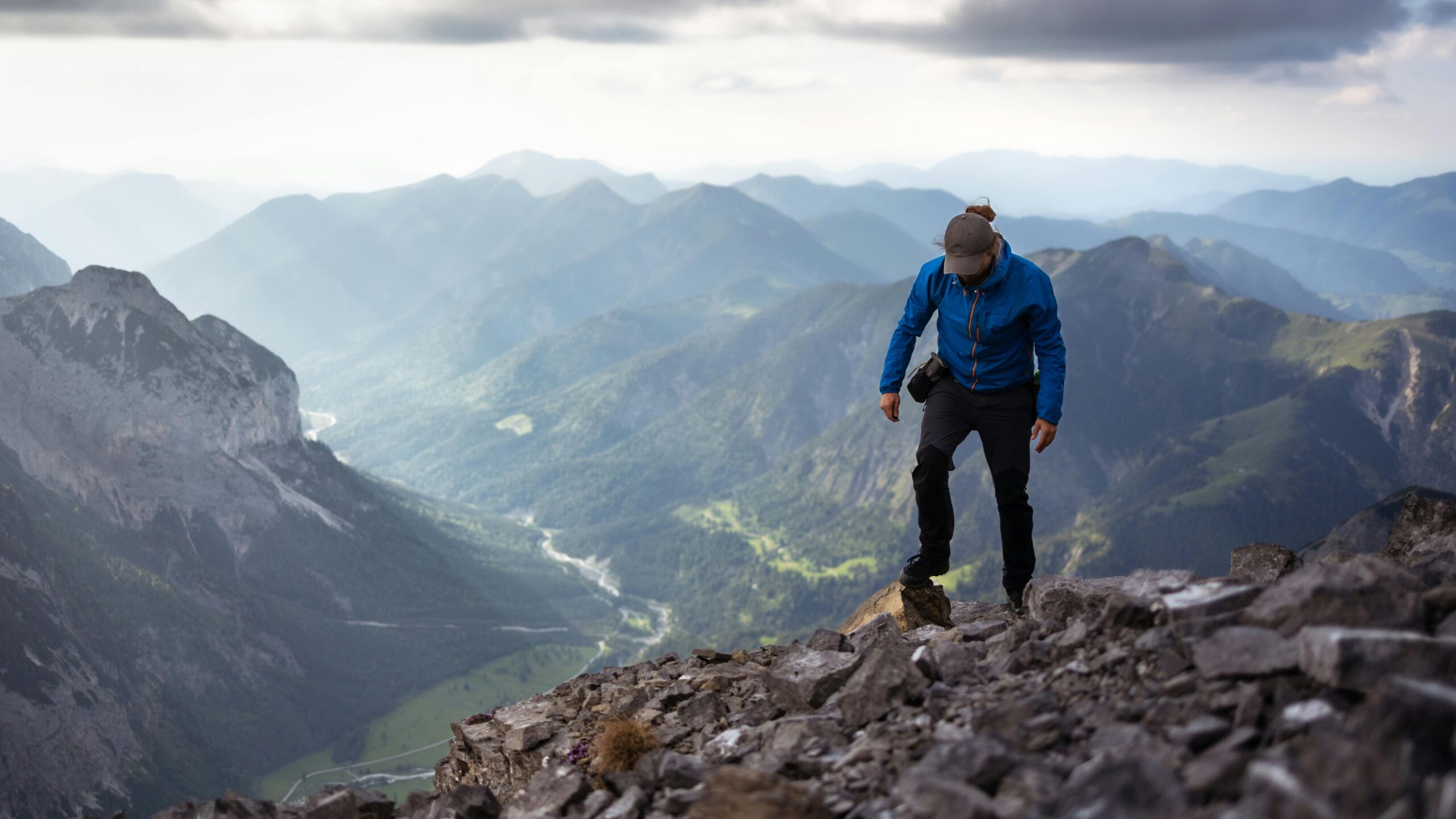A determined hiker ascends a rocky mountain trail in scenic alpine landscape.